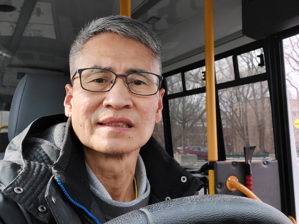 Man wearing glasses sits at steering wheel of bus working on frontline