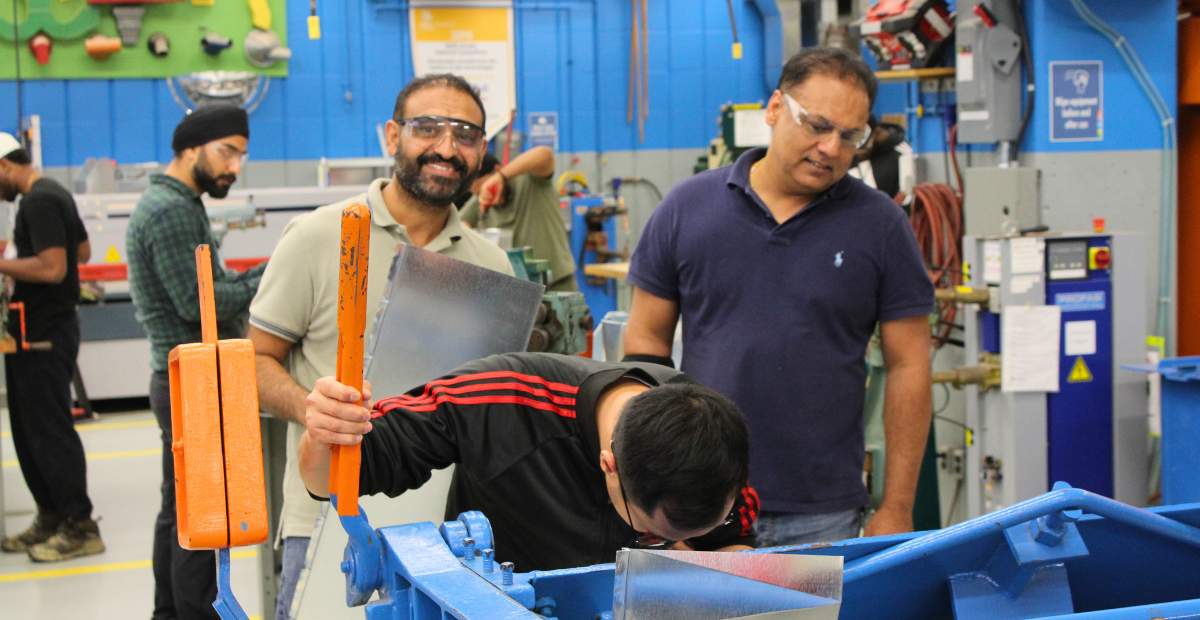 3 men work at a sheet metal press in a workshop for a plumbing apprenticeship program